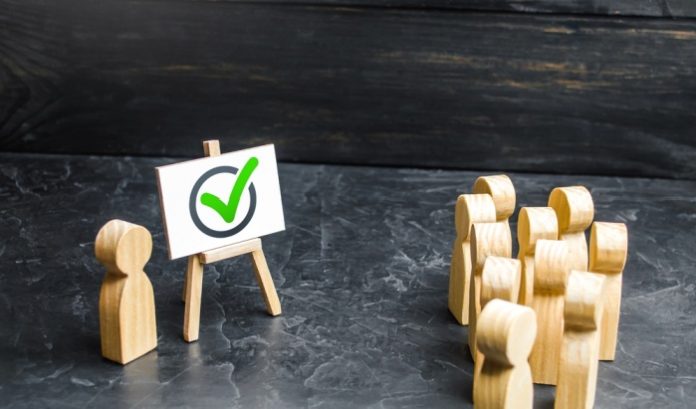 Wooden figures facing another wooden figure next to a whiteboard, concept of lobbying